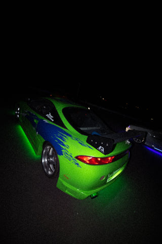 A green and blue Mitsubishi Eclipse with a large rear wing and custom decals, illuminated by green underglow lights.