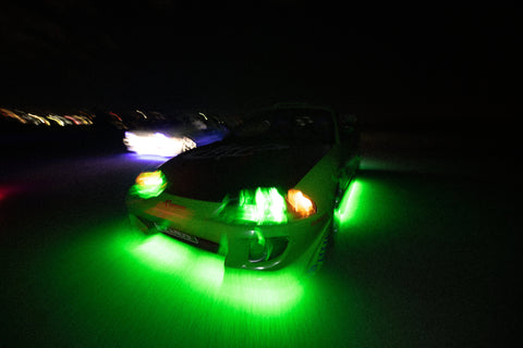 A green and blue Mitsubishi Eclipse with a large rear wing and custom decals, illuminated by green underglow lights.