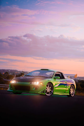 A green and blue Mitsubishi Eclipse with a large rear wing and custom decals, illuminated by green underglow lights.