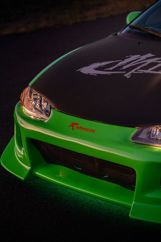 A green and blue Mitsubishi Eclipse with a large rear wing and custom decals, illuminated by green underglow lights.